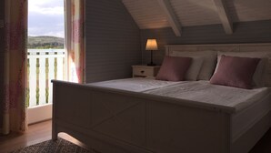 Une chambre à coucher avec un lit, une table de chevet, une lampe et une vue sur l’extérieur par une fenêtre.