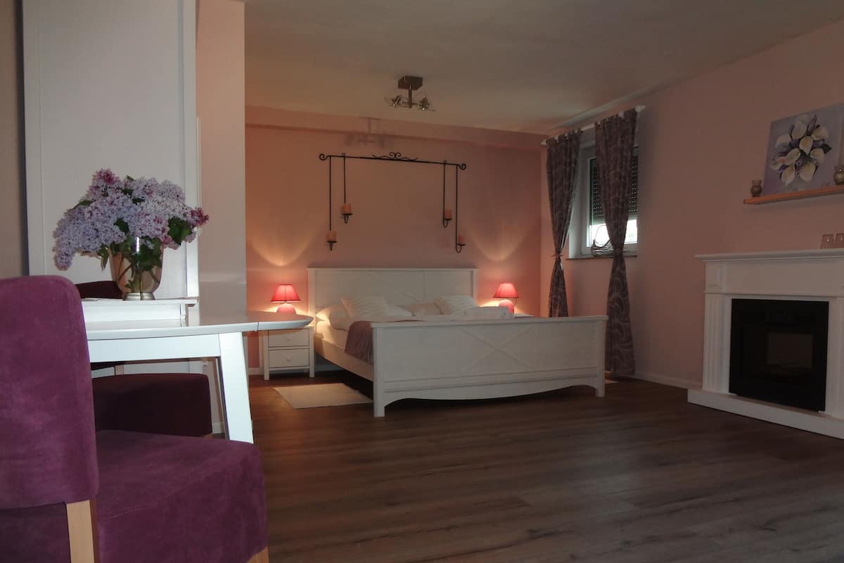 A bedroom with a bed, bedside lamps, a fireplace, and a vase of flowers.