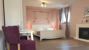 Une chambre à coucher avec un lit, des lampes de chevet, une chaise, une table et une cheminée.