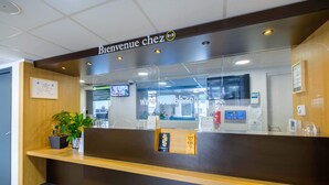 Una recepción con un cartel que dice 'Bienvenue chez', una planta en maceta y una pantalla digital.