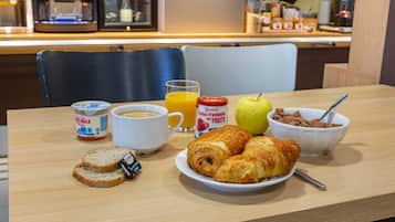 A breakfast table with croissants, a bowl of cereal, a glass of orange juice, a cup of coffee, and a jar of yogurt.