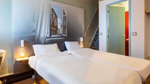 A hotel room with a large bed, a painting of a building on the wall, a nightstand with a lamp, and a staircase leading to an upper level. - B&B HOTEL CHARTRES Le Forum (1) (Le Coudray)