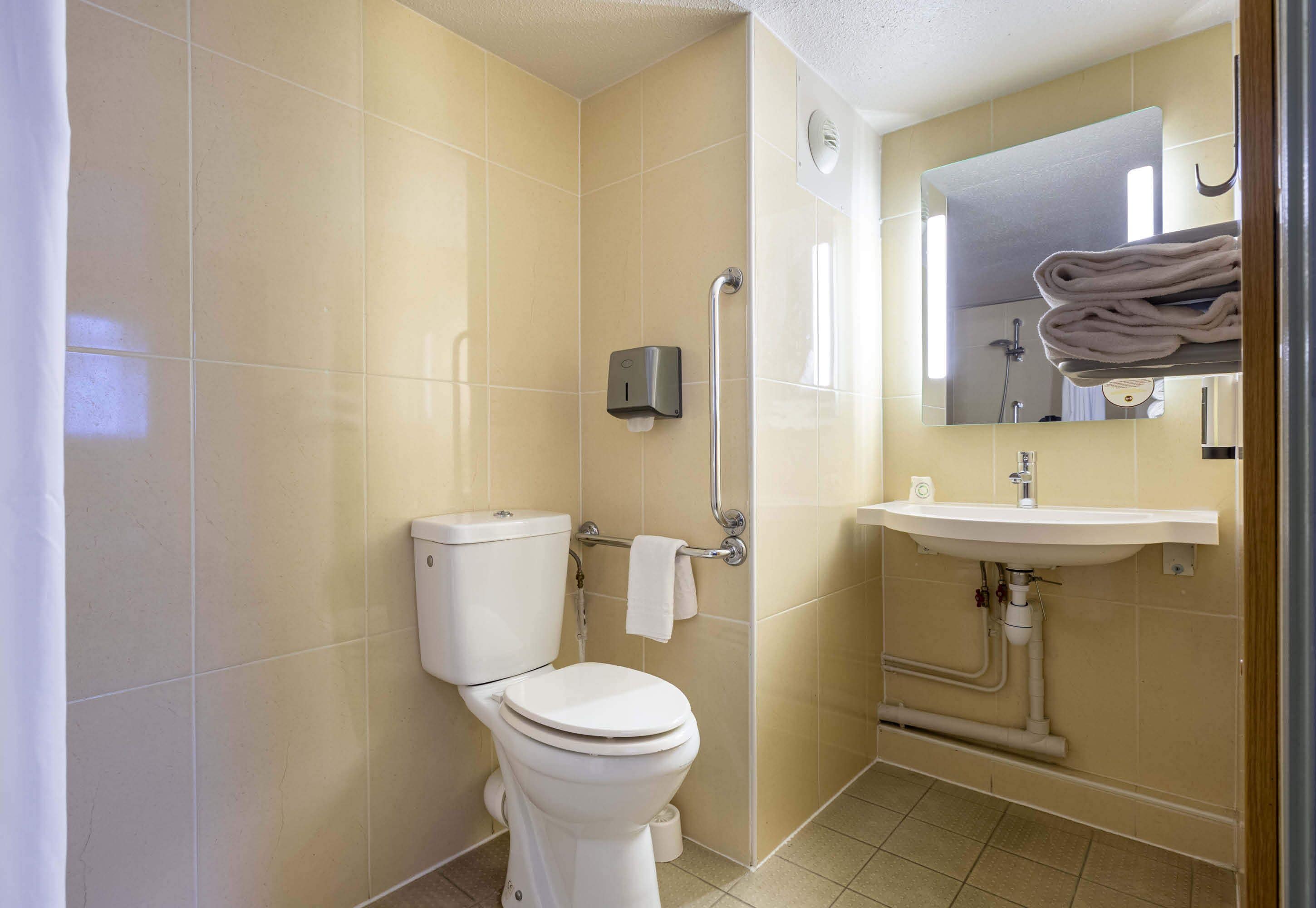 Un baño con inodoro, secamanos, lavabo y espejo.
