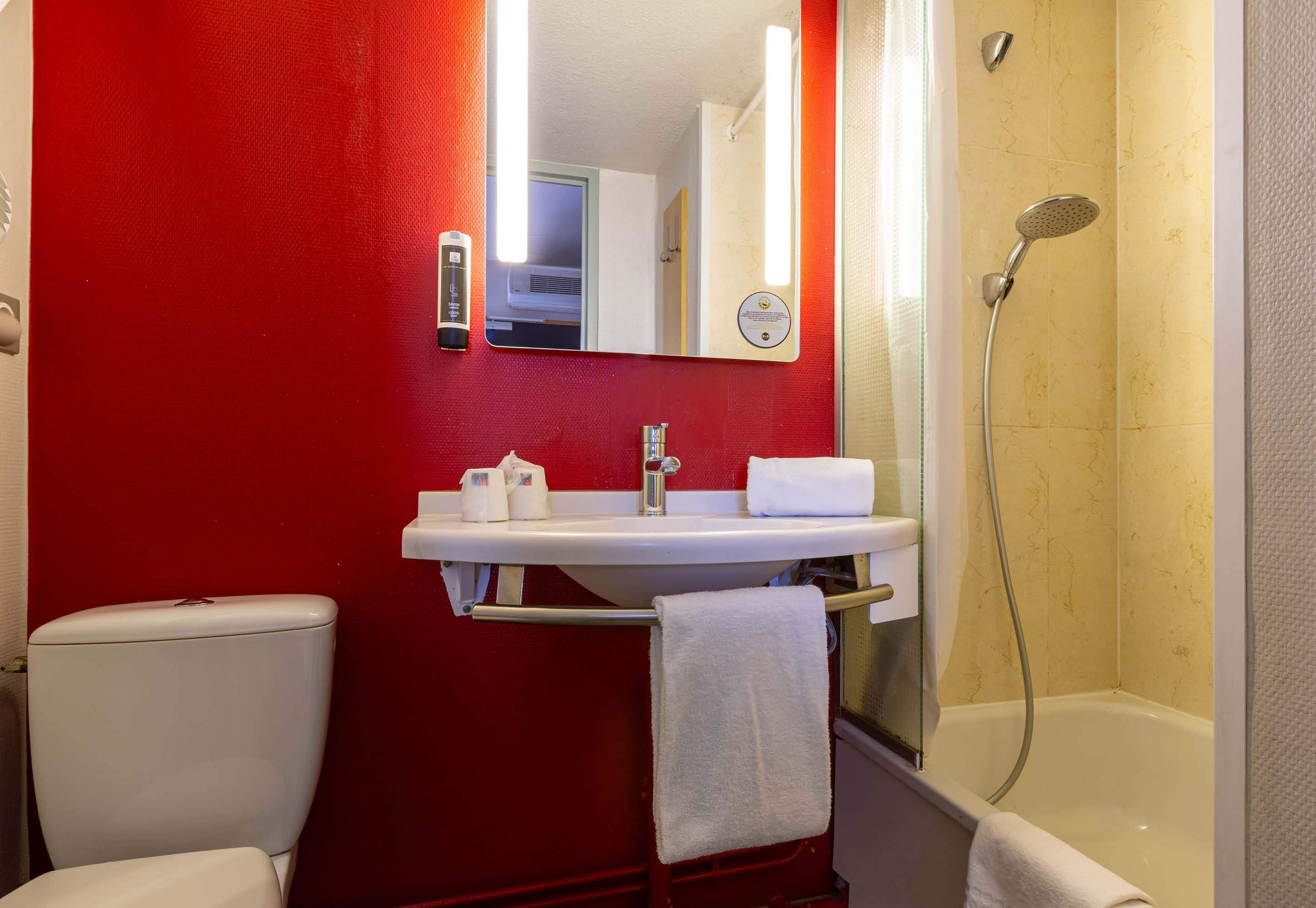 A bathroom with a red wall, white sink, and a shower.