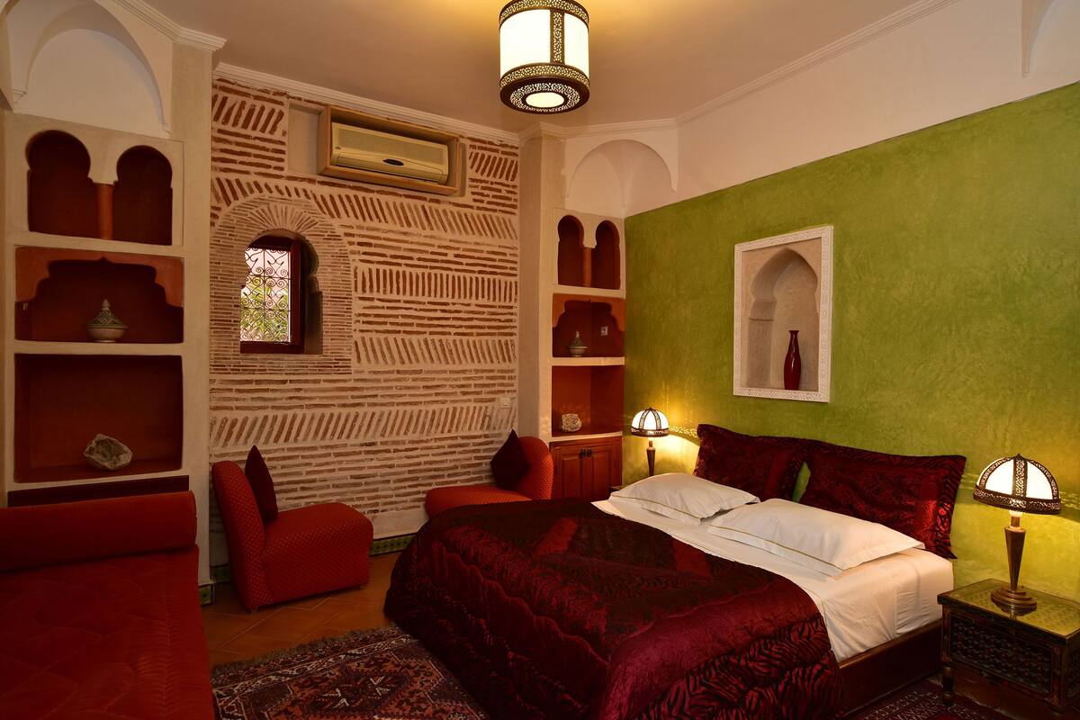 A room with a bed, red armchairs, a green wall, and a decorative archway.