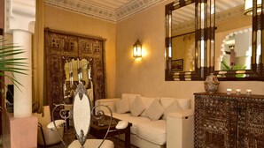 Una habitación con un sofá blanco, una silla decorativa, un armario de madera y un espejo grande.