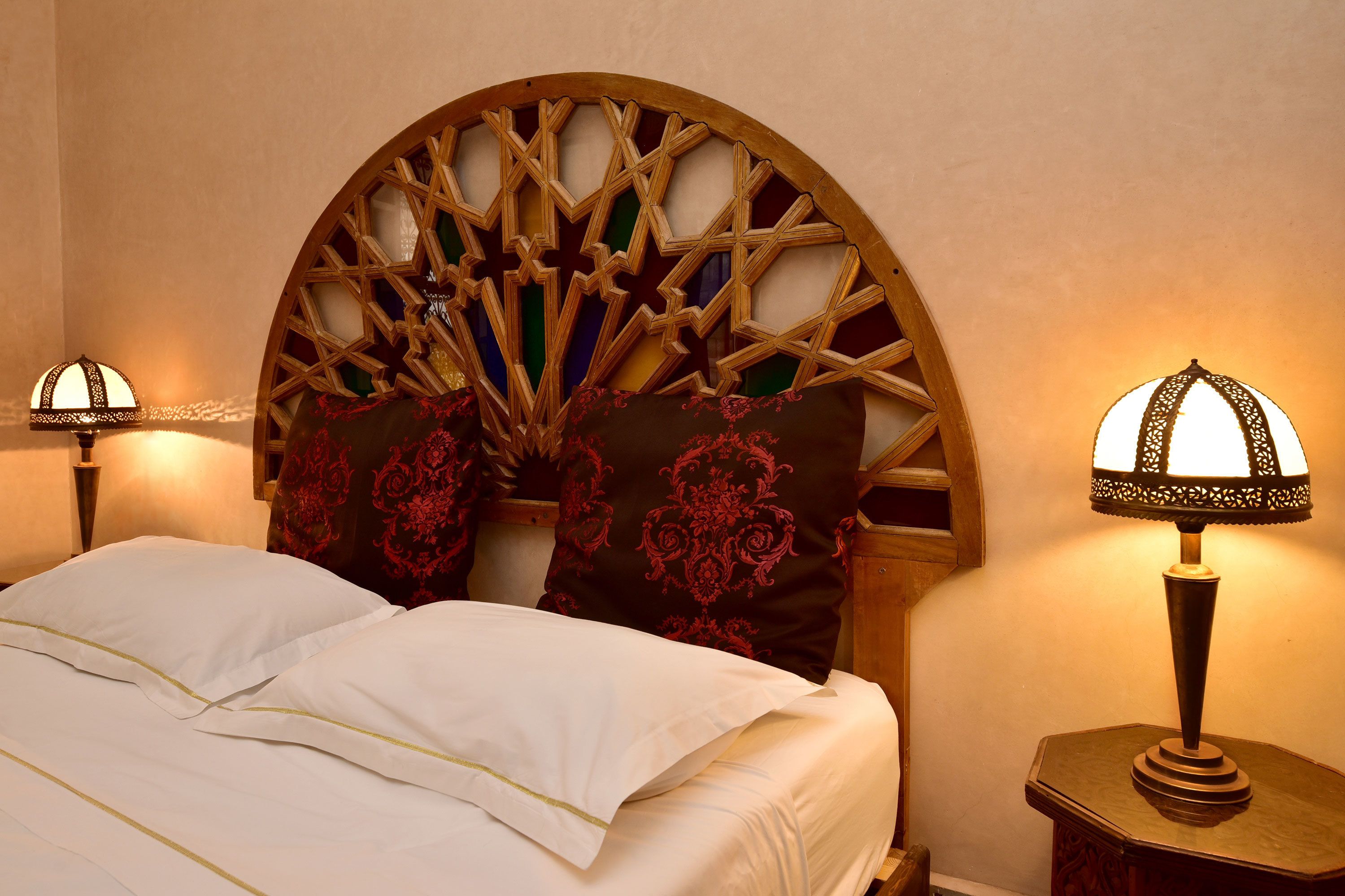 A neatly made bed with white linens and a decorative headboard with a geometric pattern. There are two bedside lamps on wooden nightstands.