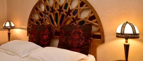 A neatly made bed with white linens and a decorative headboard with a geometric pattern. There are two bedside lamps on wooden nightstands.