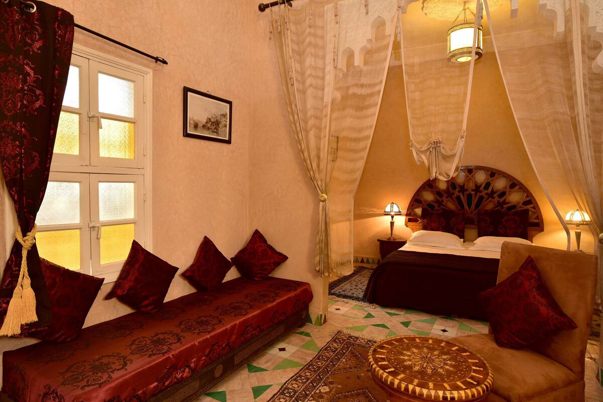 A room with a bed, a sofa, a patterned rug, and a hanging light fixture.