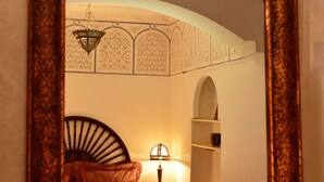 Una habitación con cama, mesita de noche, lámpara y espejo mural con diseños elaborados.