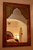 Una habitación con cama, mesita de noche, lámpara y espejo mural con diseños elaborados.