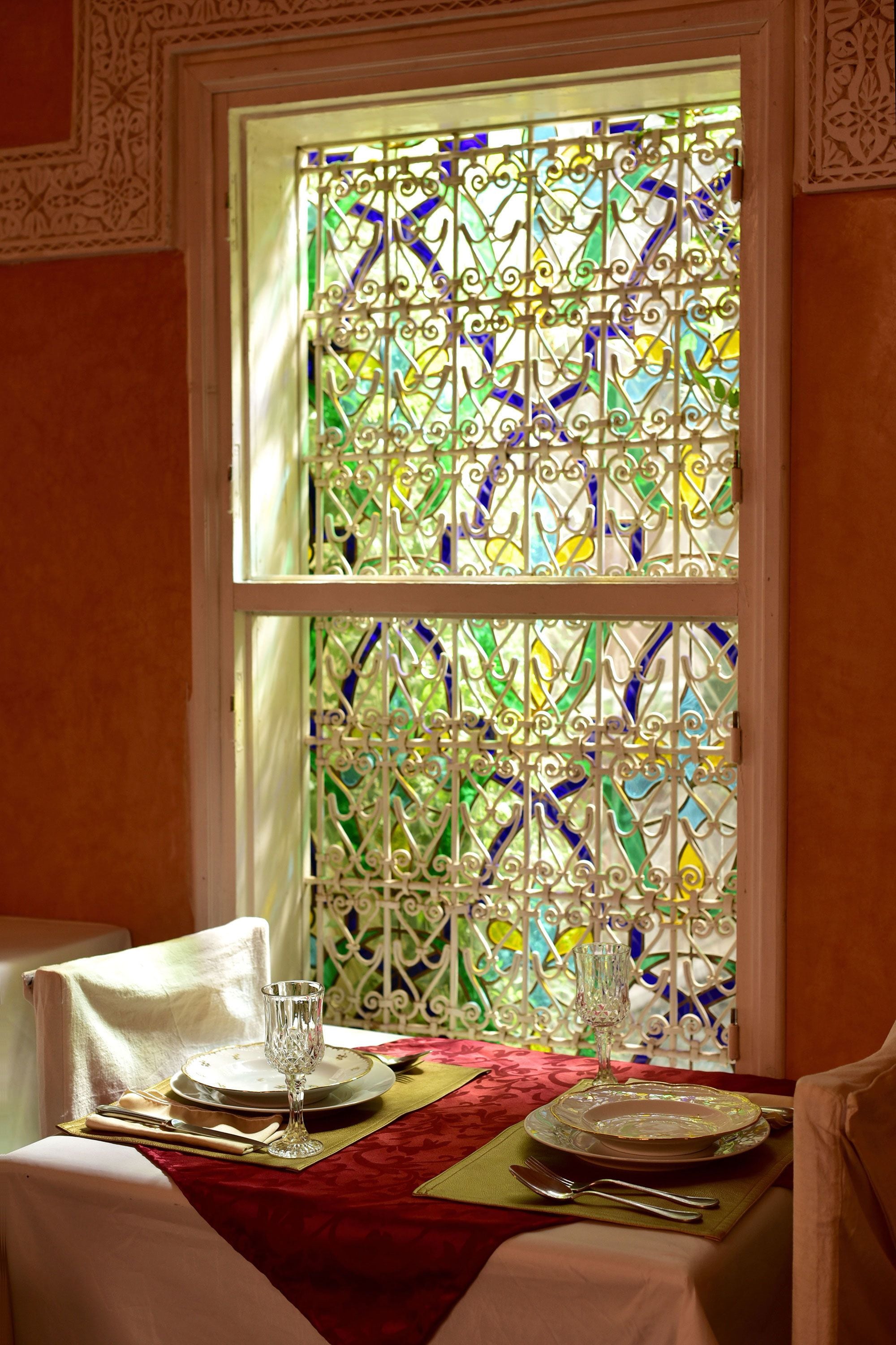 A dining table set with plates, cutlery, and a glass, positioned near a window with ornate stained glass.