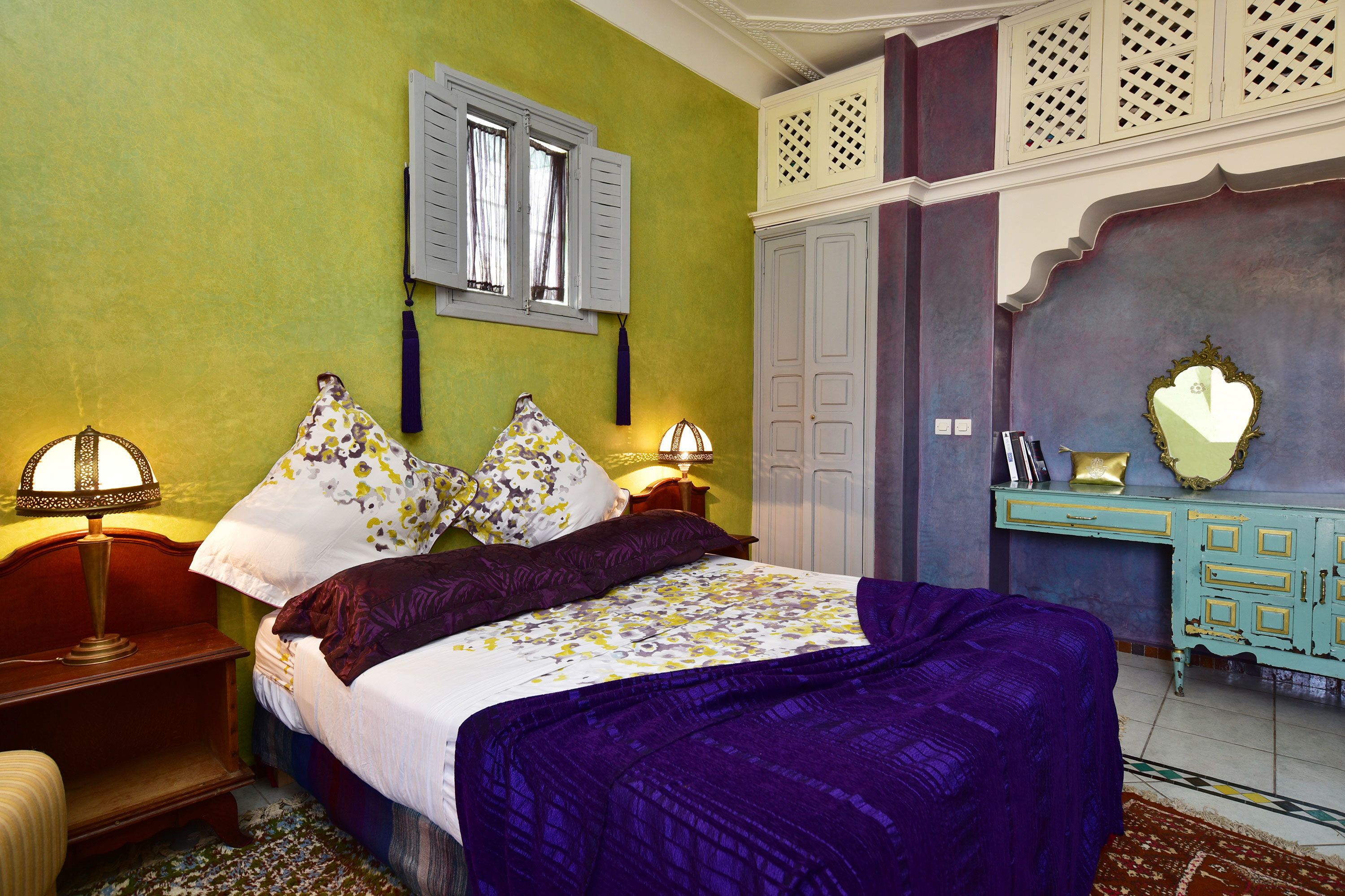 A bedroom with a bed, bedside lamps, a dresser, and a mirror.