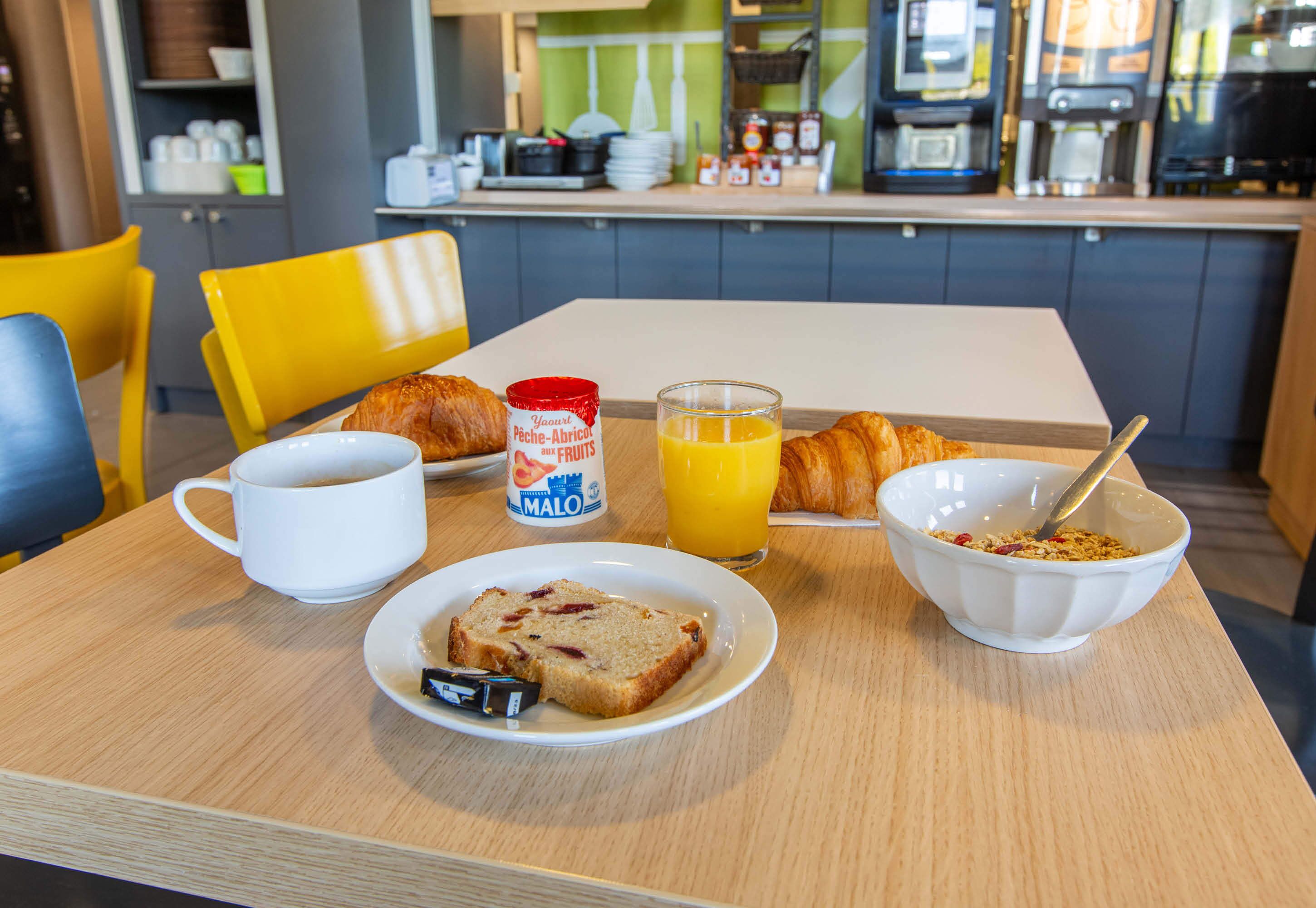 Una mesa de desayuno con cruasanes, un vaso de jugo de naranja, una taza, un plato con pan y un tazón de cereal.