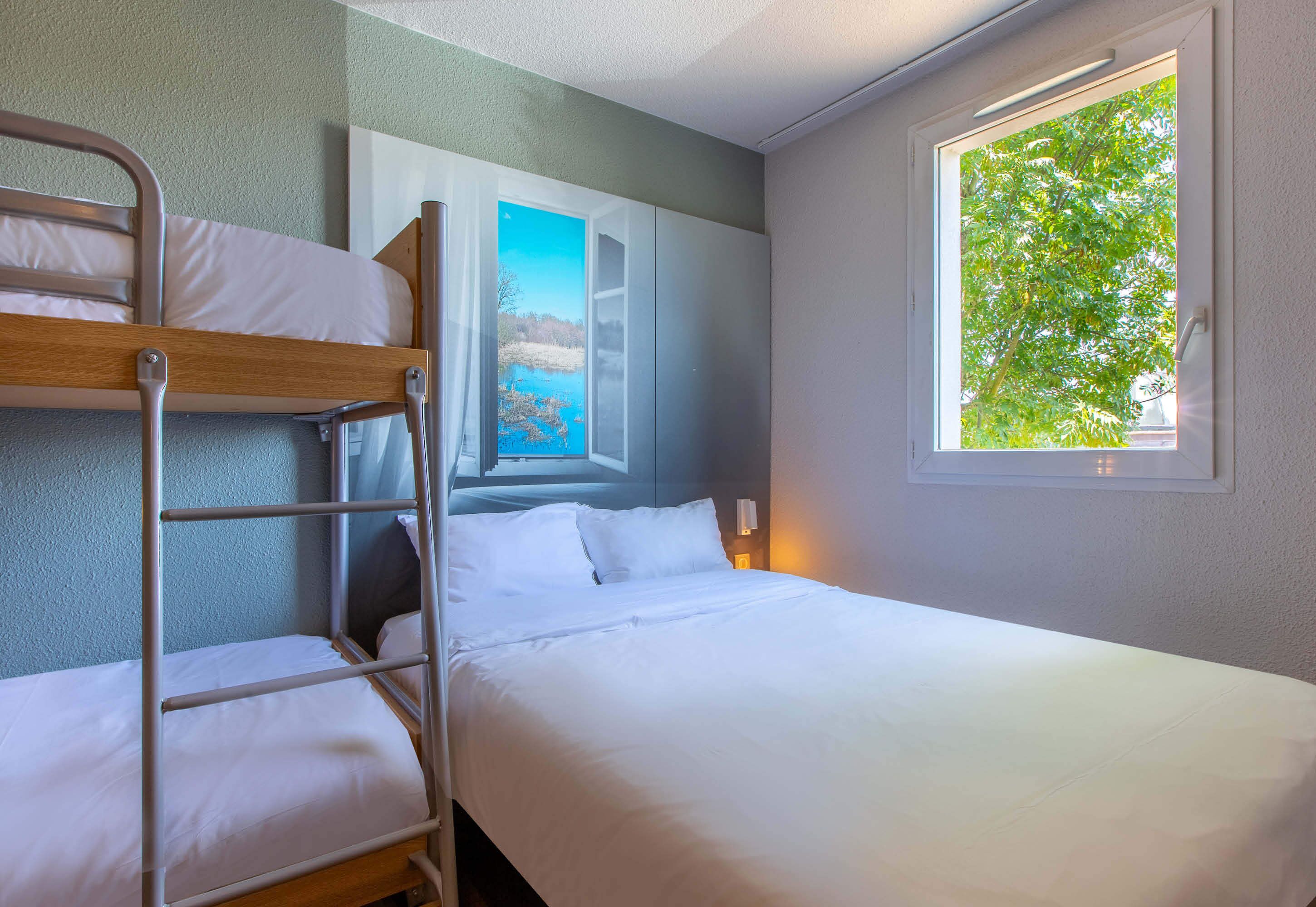 A bunk bed room with a window providing a view of greenery outside.