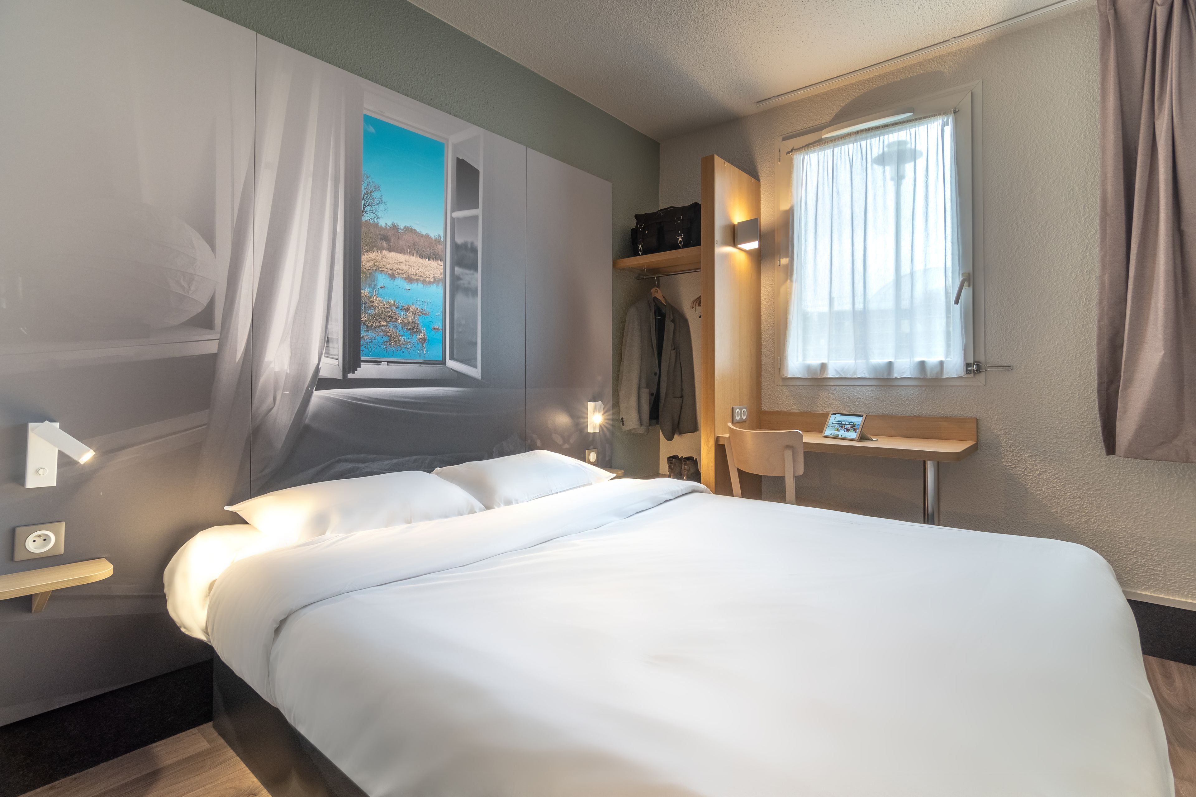 Een hotelkamer met een bed, een bureau, een stoel, een garderobe en een raam met uitzicht op een meer.