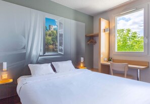 A hotel room with a bed, bedside table, lamp, chair, and a window with a view of greenery and a building. - B&B HOTEL Châteauroux Déols (Deols)