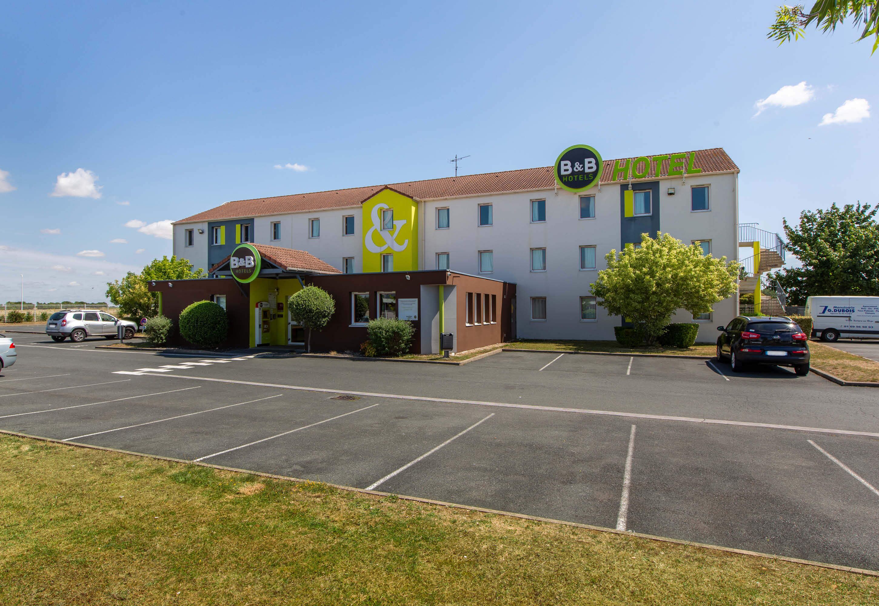 A B&B hotel with a parking lot and a small building with a green sign.