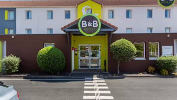 Un hôtel de type « bed and breakfast » avec une façade jaune, deux arbustes ronds et un ciel dégagé.