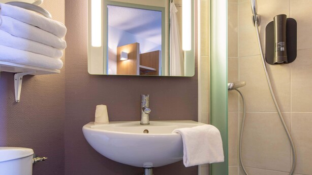 Ein Badezimmer mit Waschbecken, Spiegel, Handtuchhalter und Dusche.
