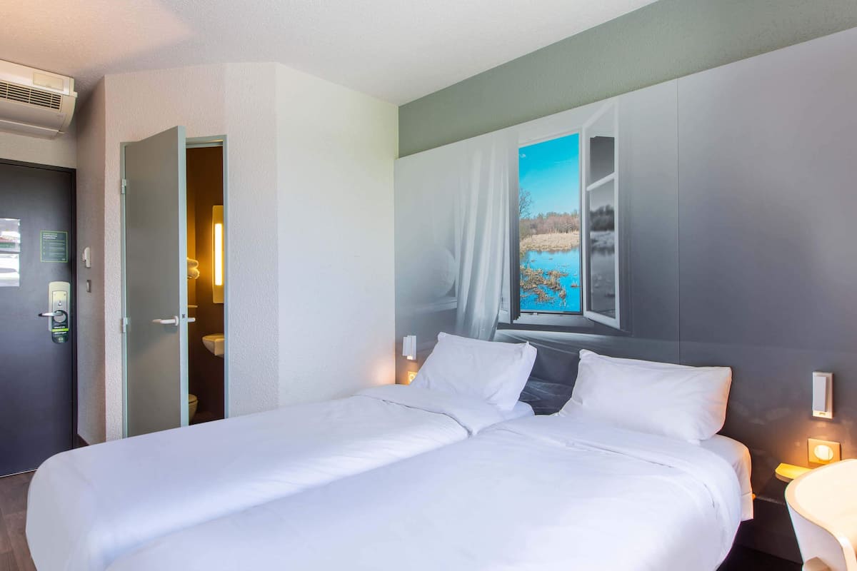 Ein Hotelzimmer mit einem großen Bett, einem durchgegangenen Tür erkennbaren Badezimmer und einem Landschaftsbild an der Wand.