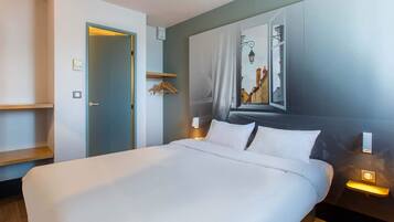 A modern hotel room with a large bed, a wardrobe, a mirror, and a wall-mounted light fixture.