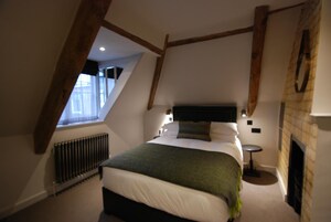 A bedroom with a sloped ceiling, a bed with a green blanket, a small round table, and a fireplace.