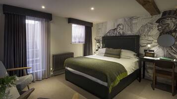 A bedroom with a large bed, a desk, a chair, a radiator, and a window with curtains.