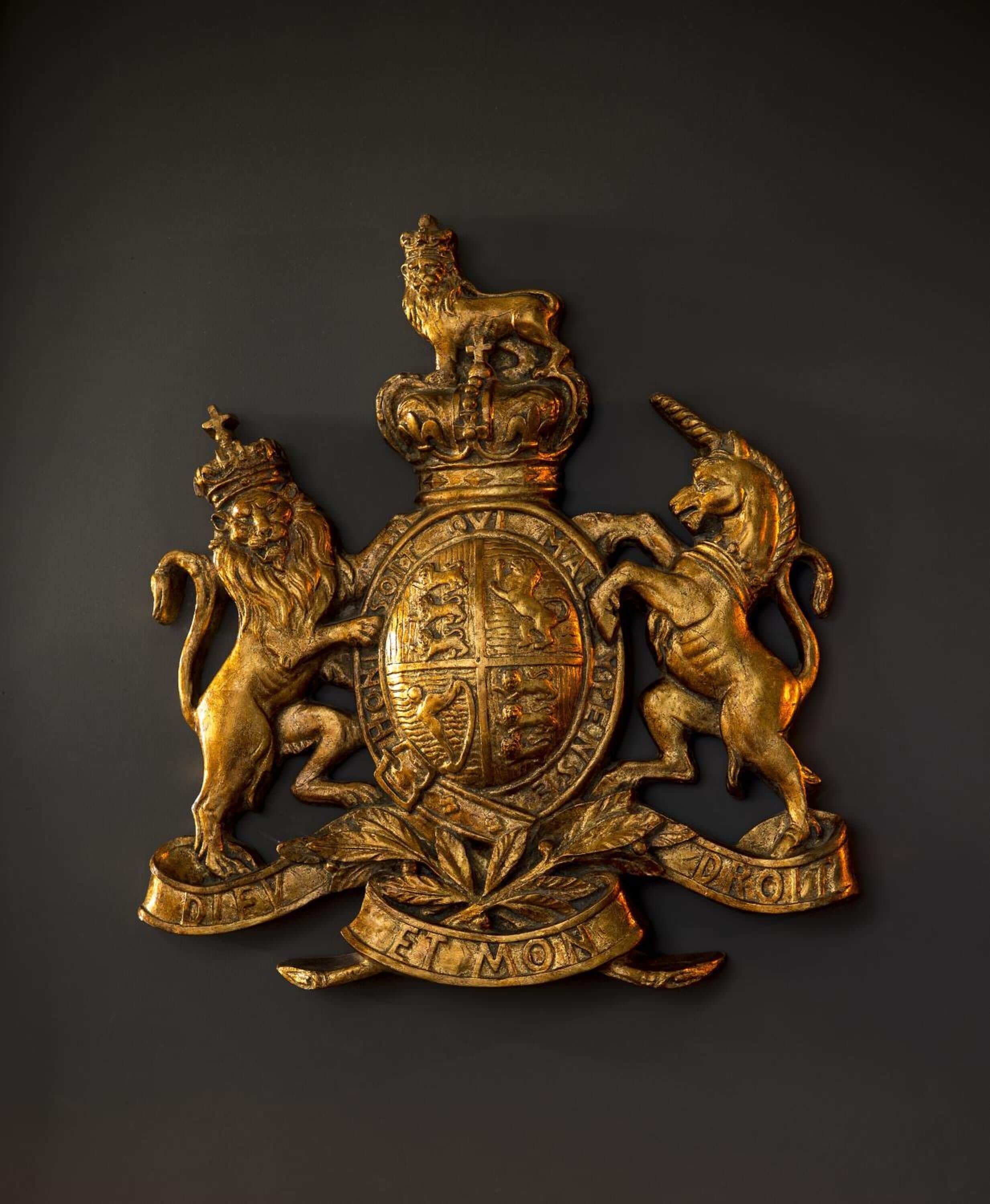 A gold-colored coat of arms with a shield, two lions, and a crown.
