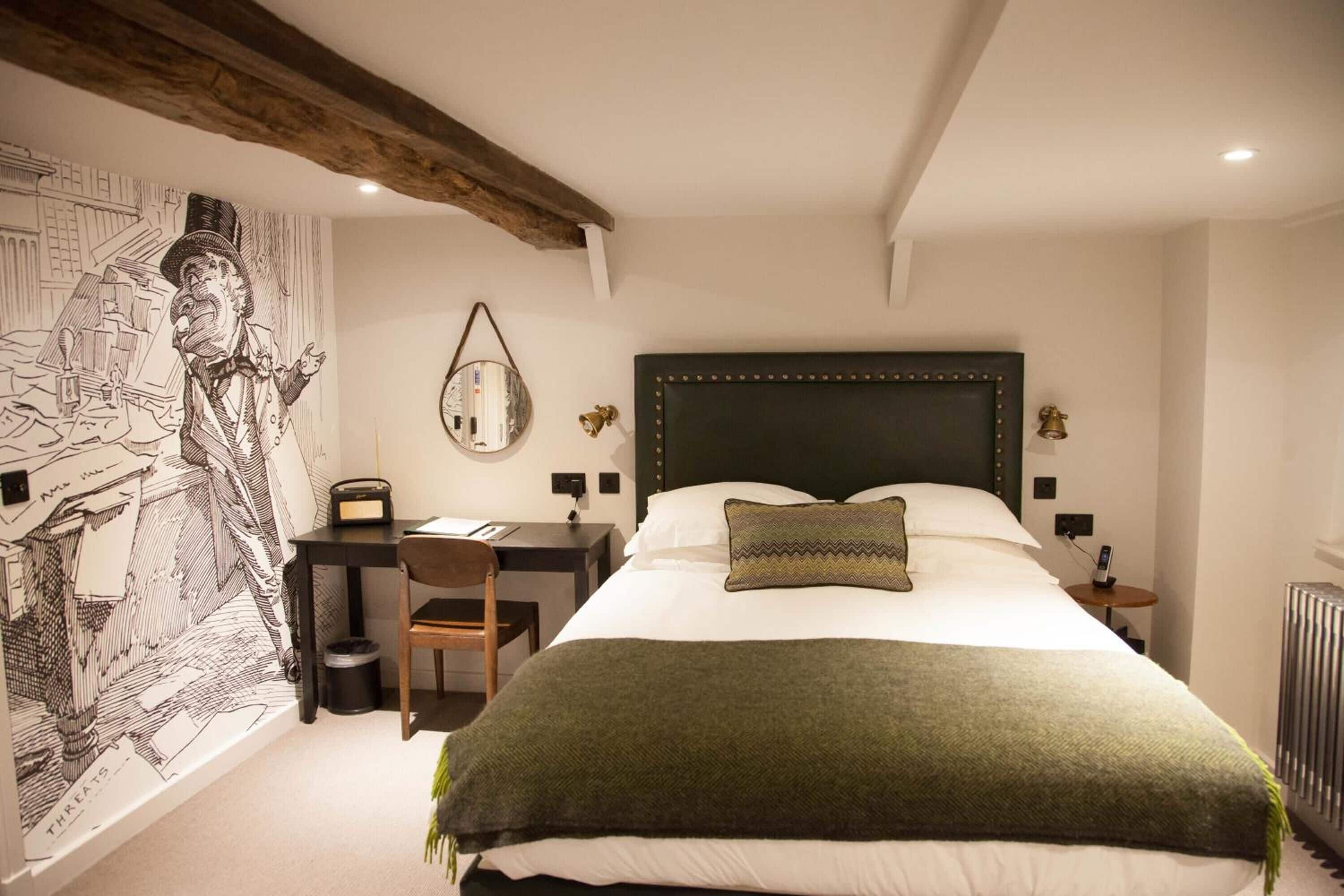 A bedroom with a large bed, a desk, and a chair. There is a wall with a mural and a radiator.