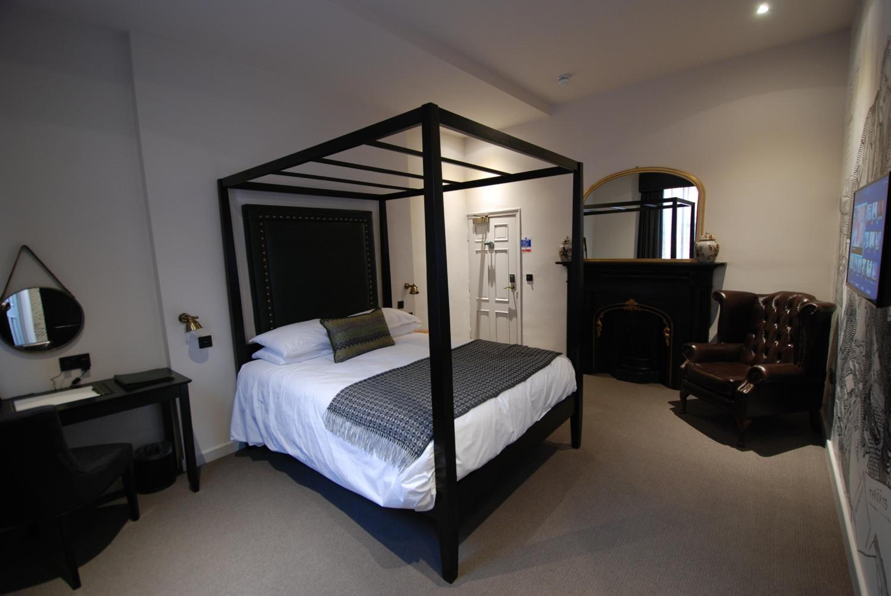 Un lit à baldaquin avec un cadre sombre, un bureau avec une chaise, une cheminée et un miroir au mur.
