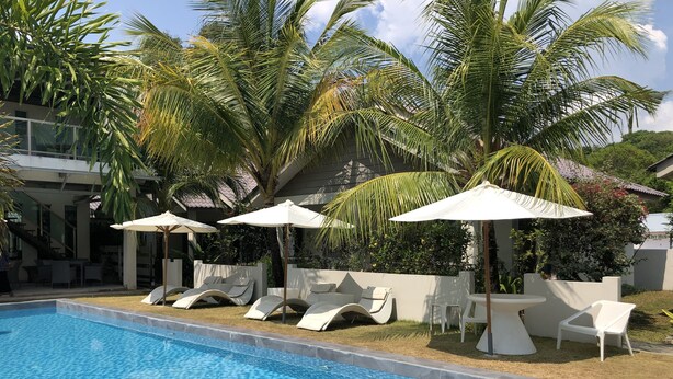 A swimming pool with lounge chairs and umbrellas, surrounded by palm trees and a building. - Fuuka Villa (Langkawi)