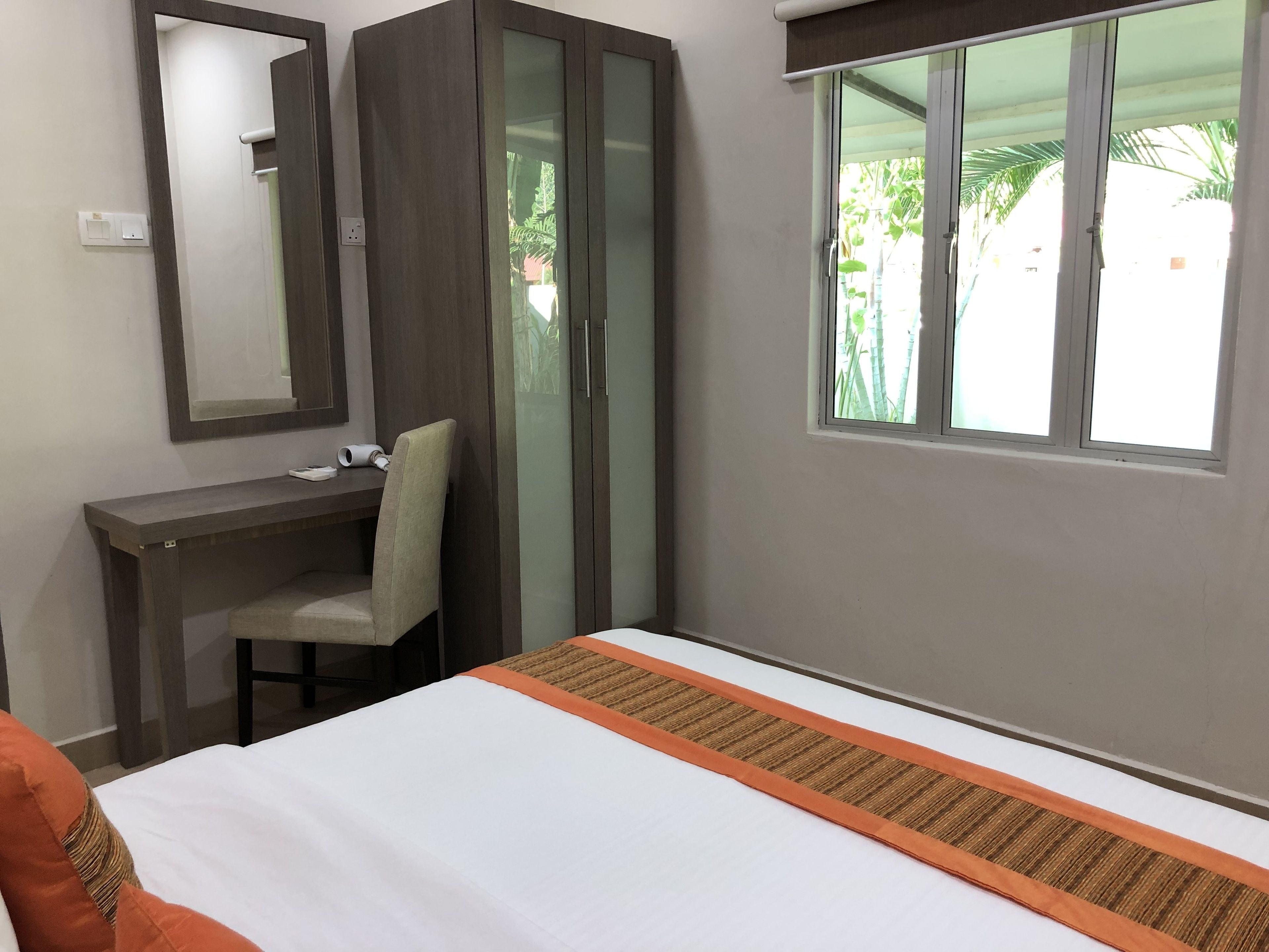 A hotel room with a bed, a desk, a chair, a wardrobe, and a window with a view of greenery.