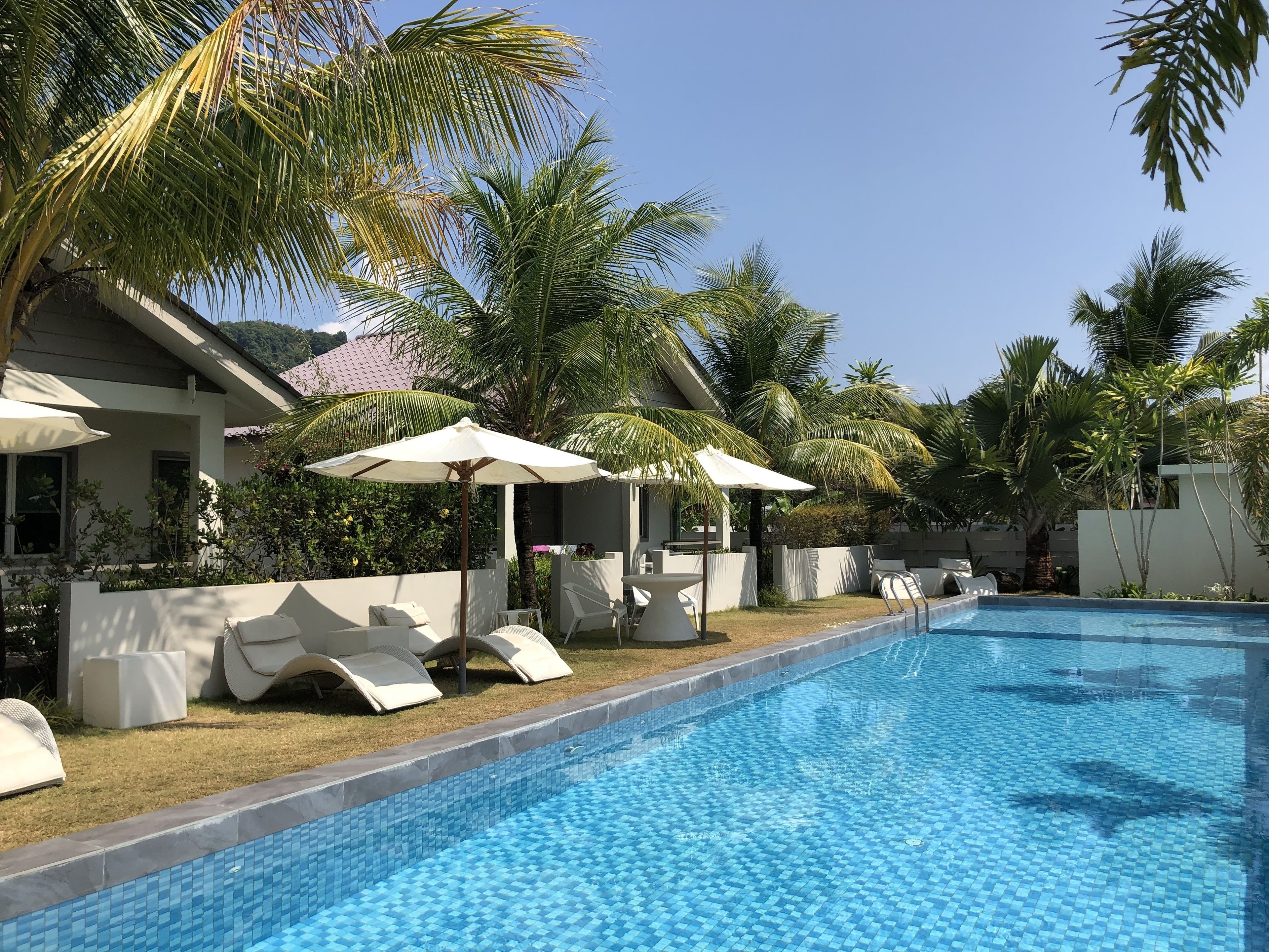A swimming pool with lounge chairs and umbrellas, surrounded by palm trees and a modern building.