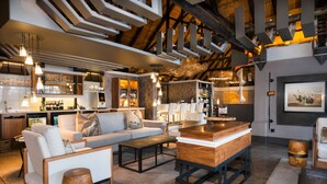 A modern interior with a sofa set, wooden coffee table, and a bar area with shelves of bottles. - Chobe Water Villas (Kasika)