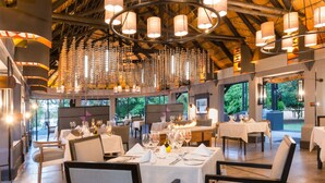 A spacious dining area with high ceilings and hanging pendant lights. Tables are set with white tablecloths and chairs. - Chobe Water Villas (Kasika)