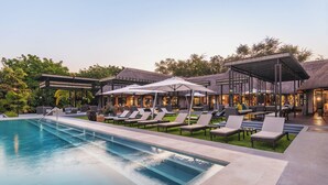 A poolside area with lounge chairs and umbrellas, a pool, and a building with a thatched roof. - Chobe Water Villas (Kasika)