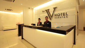 Una recepción de hotel de diseño moderno, un gran logotipo iluminado en forma de 'V' y dos empleados.