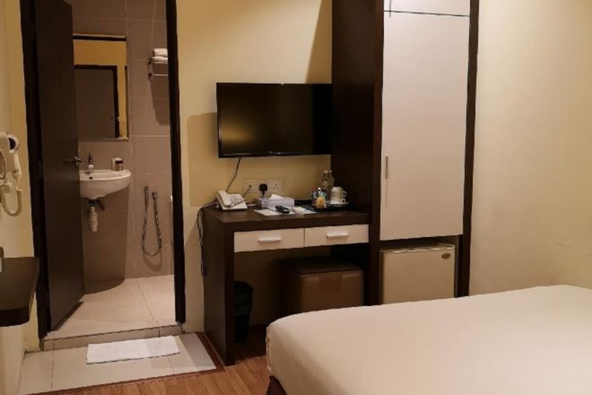 A hotel room with a bed, a desk with a telephone, a TV, a sink, and a mirror.