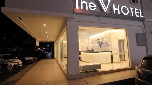 El V Hotel, con fachada moderna, grandes ventanales de vidrio y una entrada bien iluminada.