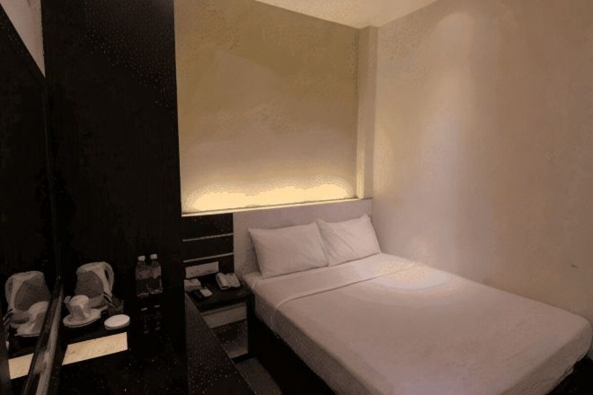 A hotel room with a single bed, bedside table, lamp, and a mirror.