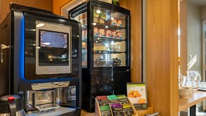 A coffee machine, a refrigerated display case with snacks, and a tray of coffee pods.