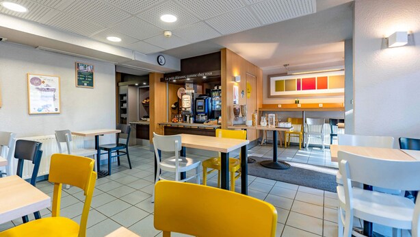 A restaurant with multiple tables and chairs, a counter with a menu, and a clock on the wall.