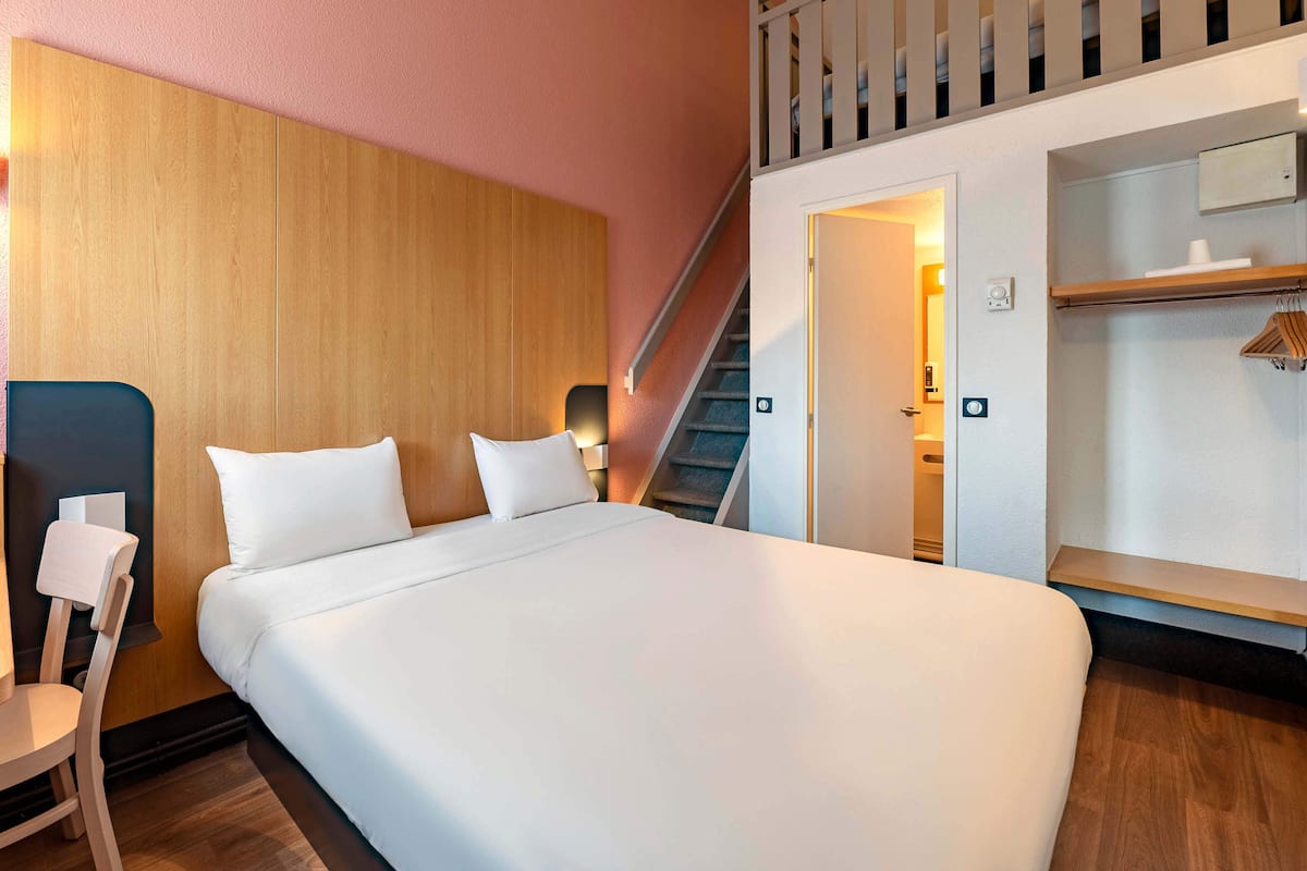 Habitación de hotel con una cama grande, cabecera de madera, una silla, un escritorio, un armario y una escalera que lleva a un nivel superior.