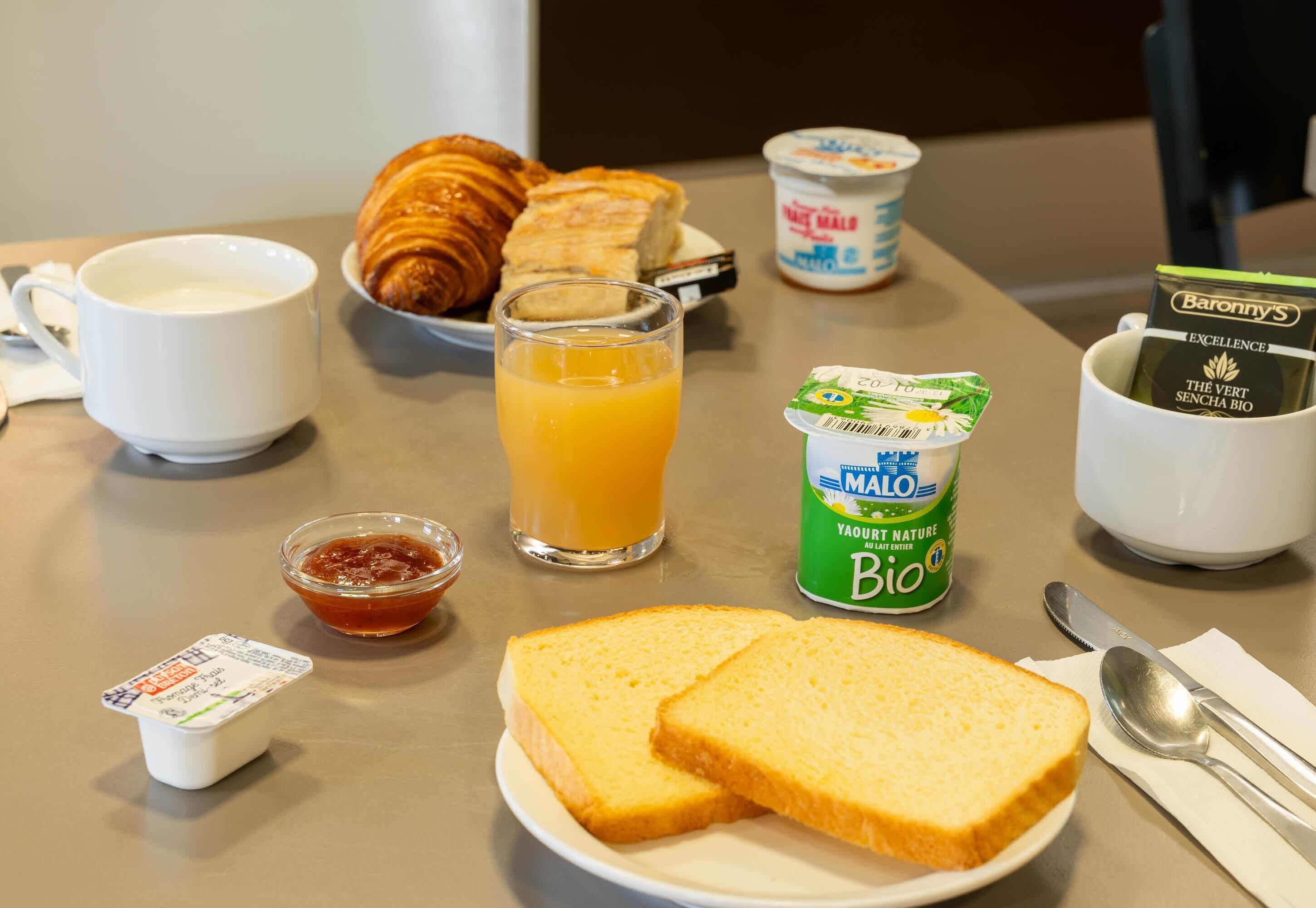 Una mesa de desayuno con cruasanes, tostadas, jugo, yogur y café.
