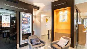 Un hall d’hôtel moderne doté de distributeurs automatiques, d’espaces de détente et d’un comptoir d’accueil.