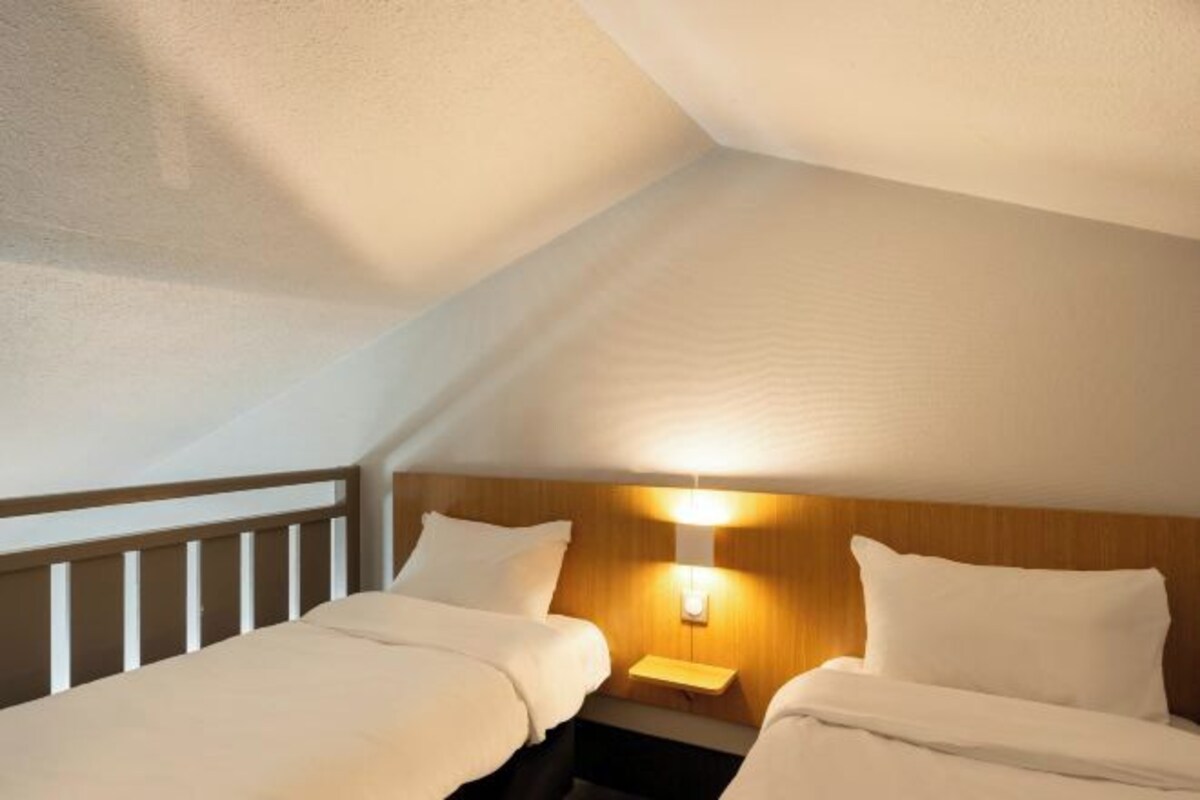 A bedroom with two beds, a nightstand, and a wall-mounted light.