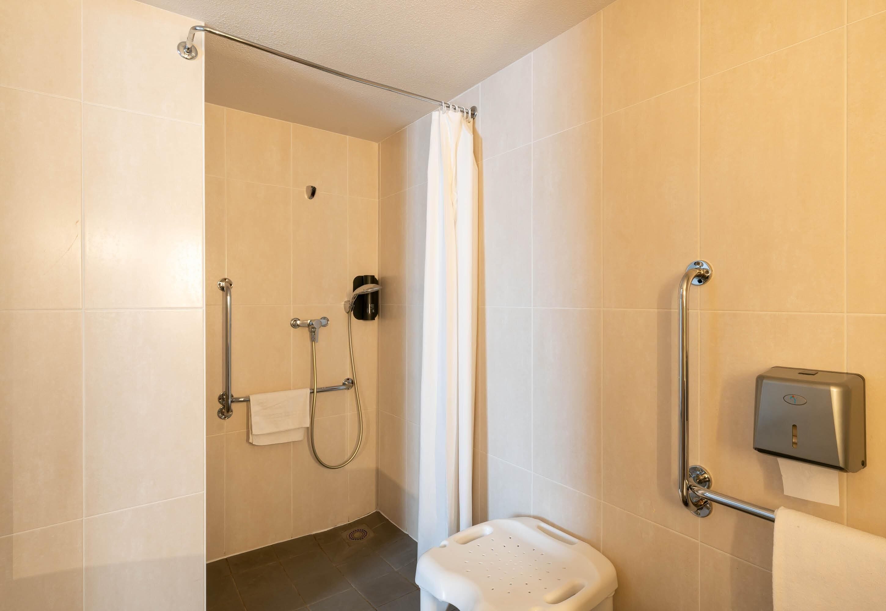 A bathroom with a shower, toilet, grab bar, and towel dispenser.