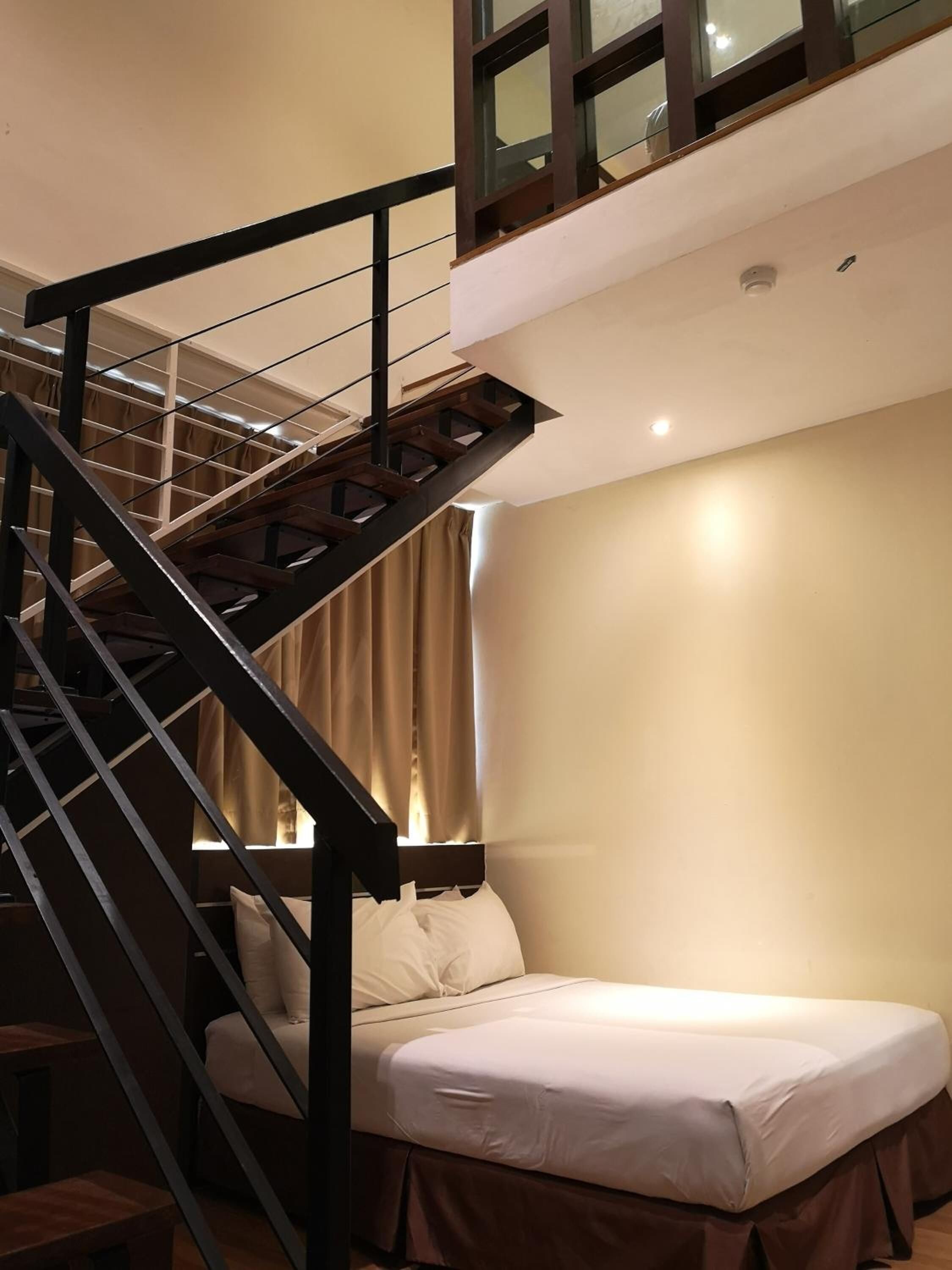 A bedroom with a bed, a staircase, and a window with curtains.