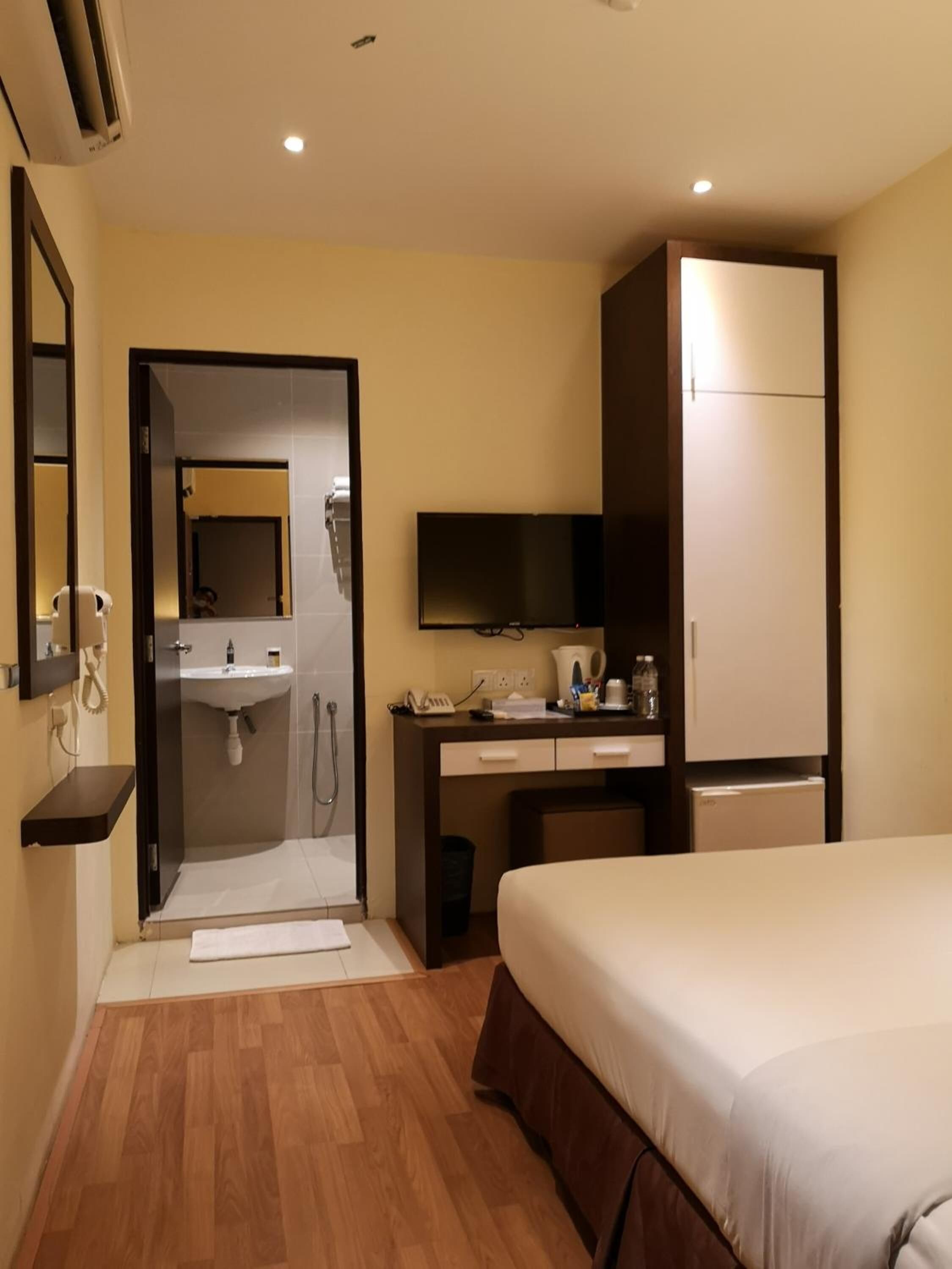 A hotel room with a bed, a desk with a flat-screen TV, a mirror, a sink, and a wardrobe.